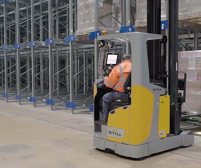 Un carrello elevatore giallo fra gli scaffali alti del magazzino automatizzato