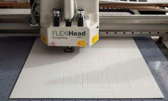 Il plotter da taglio che incide una fustella su un foglio di cartone bianco